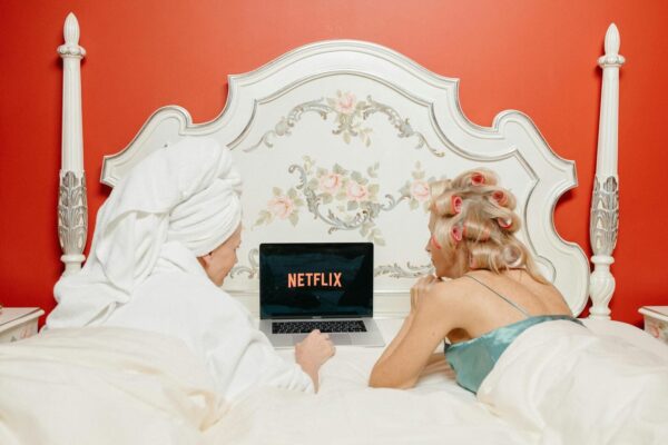 Dvije žene leže na krevetu, a ispred njih je laptop na kojem je logo od Netflixa.