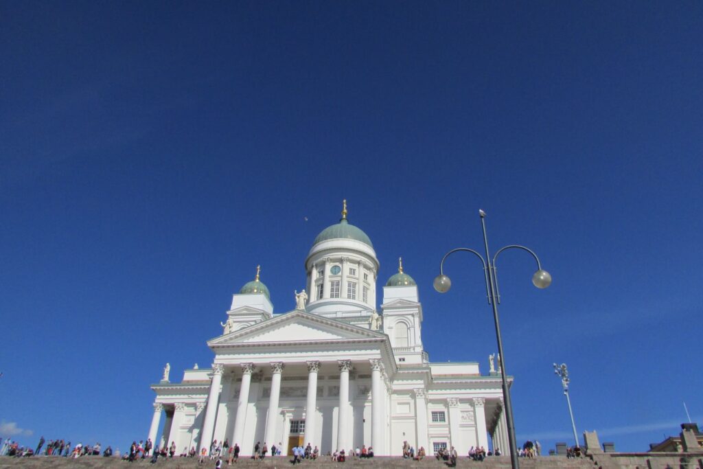 Bijela katedrala s tri tirkizne kupole u Helsinkiju sa plavim nebom kao pozadinom.