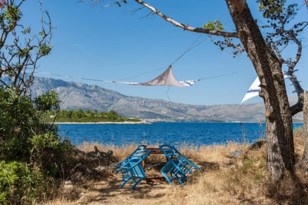 Četiri plava stolca naslonjena na drveni stol s morem i planinama u pozadini na otoku Vrnik u Hrvatskoj.