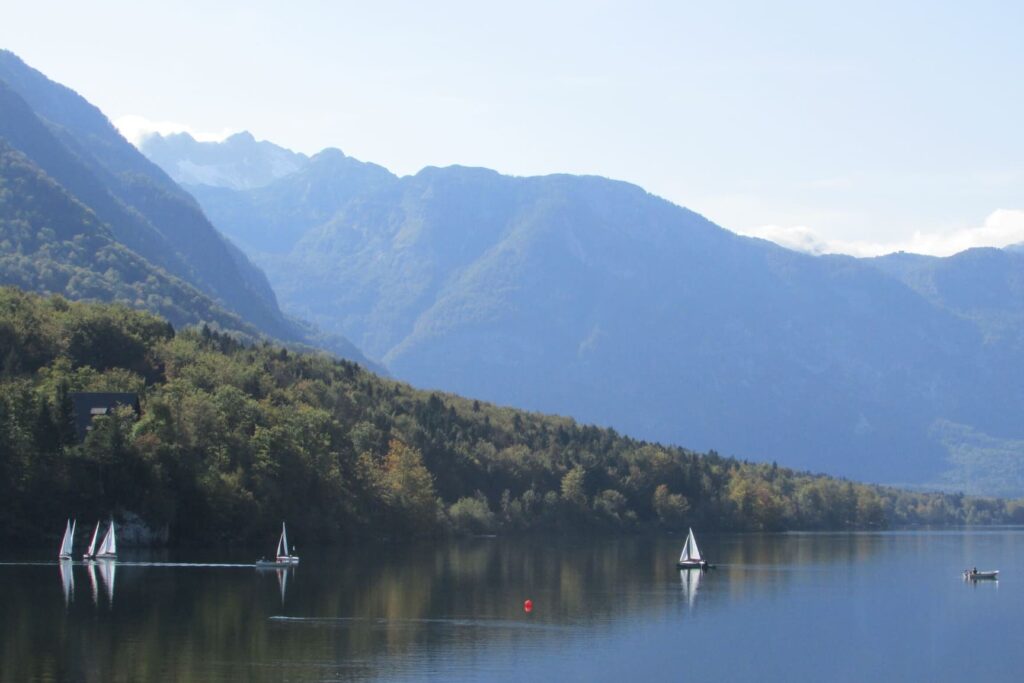 Bijele jedrilice u jezeru Bohinj okruženim brdima i planinama u Sloveniji.